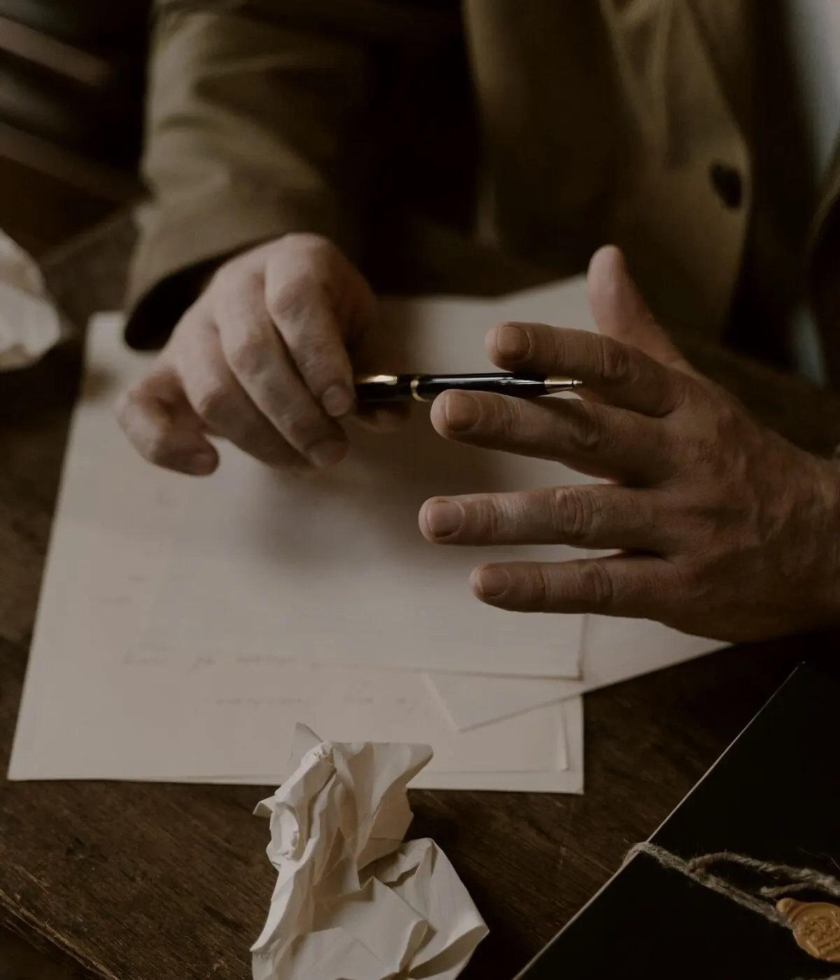 Vista de cima de uma mesa de madeira com documentos, papéis anotados e uma caneta entre as mãos
